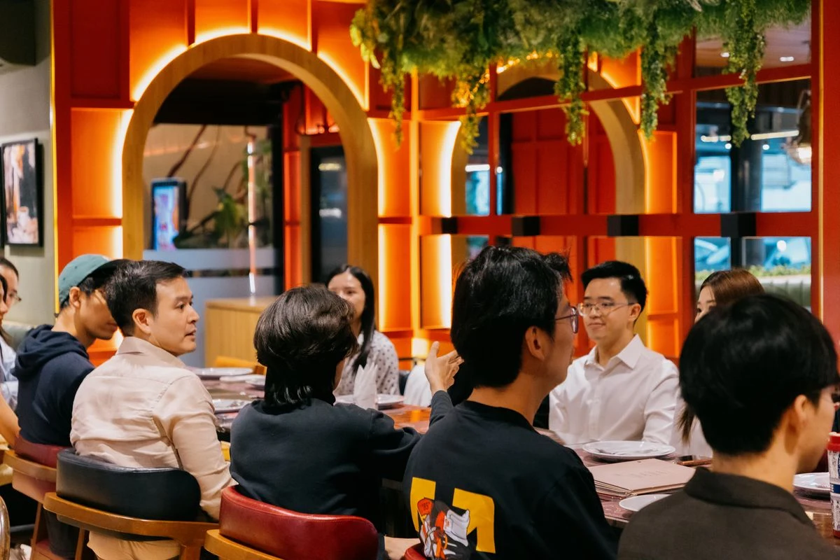 Members deep in conversation at the dinner table, orange interior at OAK Bangkok